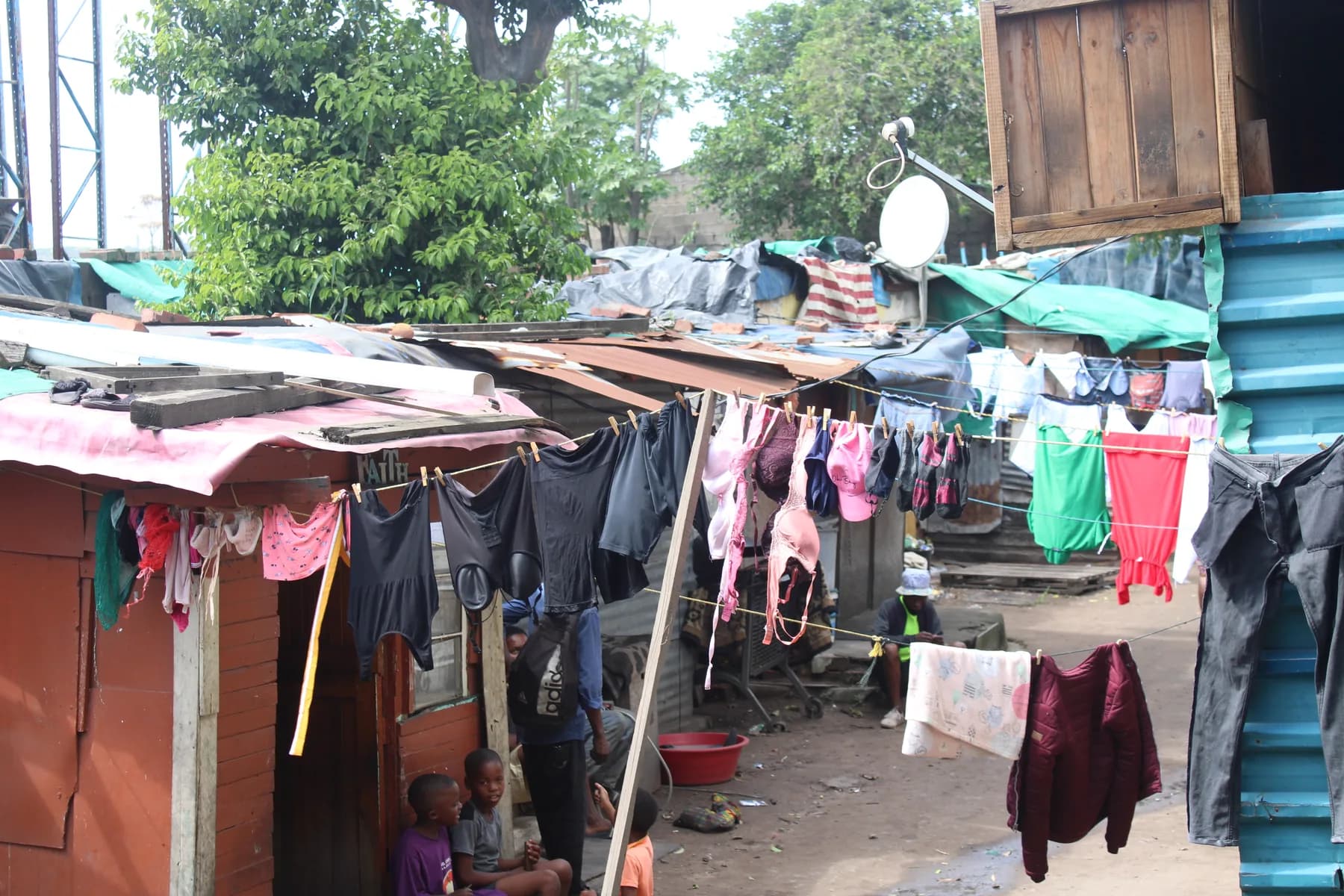 Washing strung between shacks, with children sitting in a doorway below it
