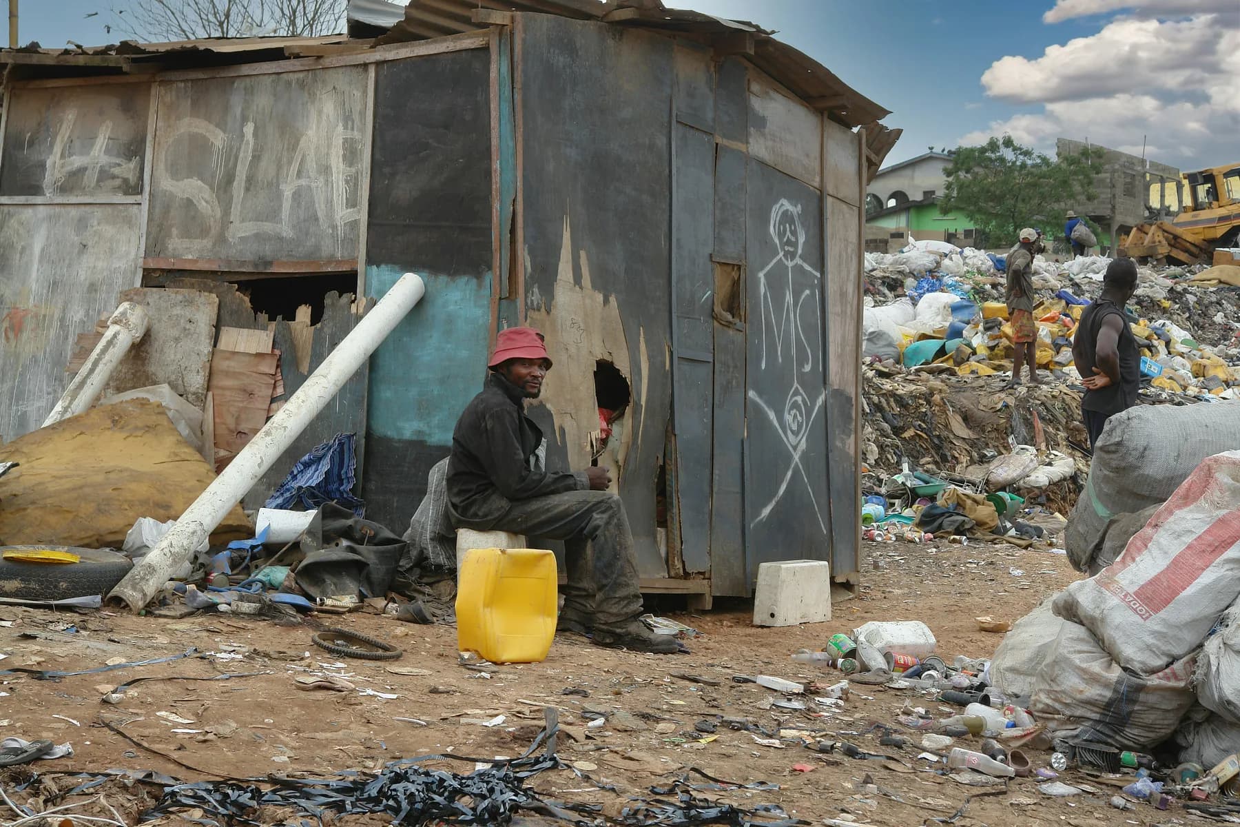 A man sitting outside a corrugated-iron shack beside a rubbish tip