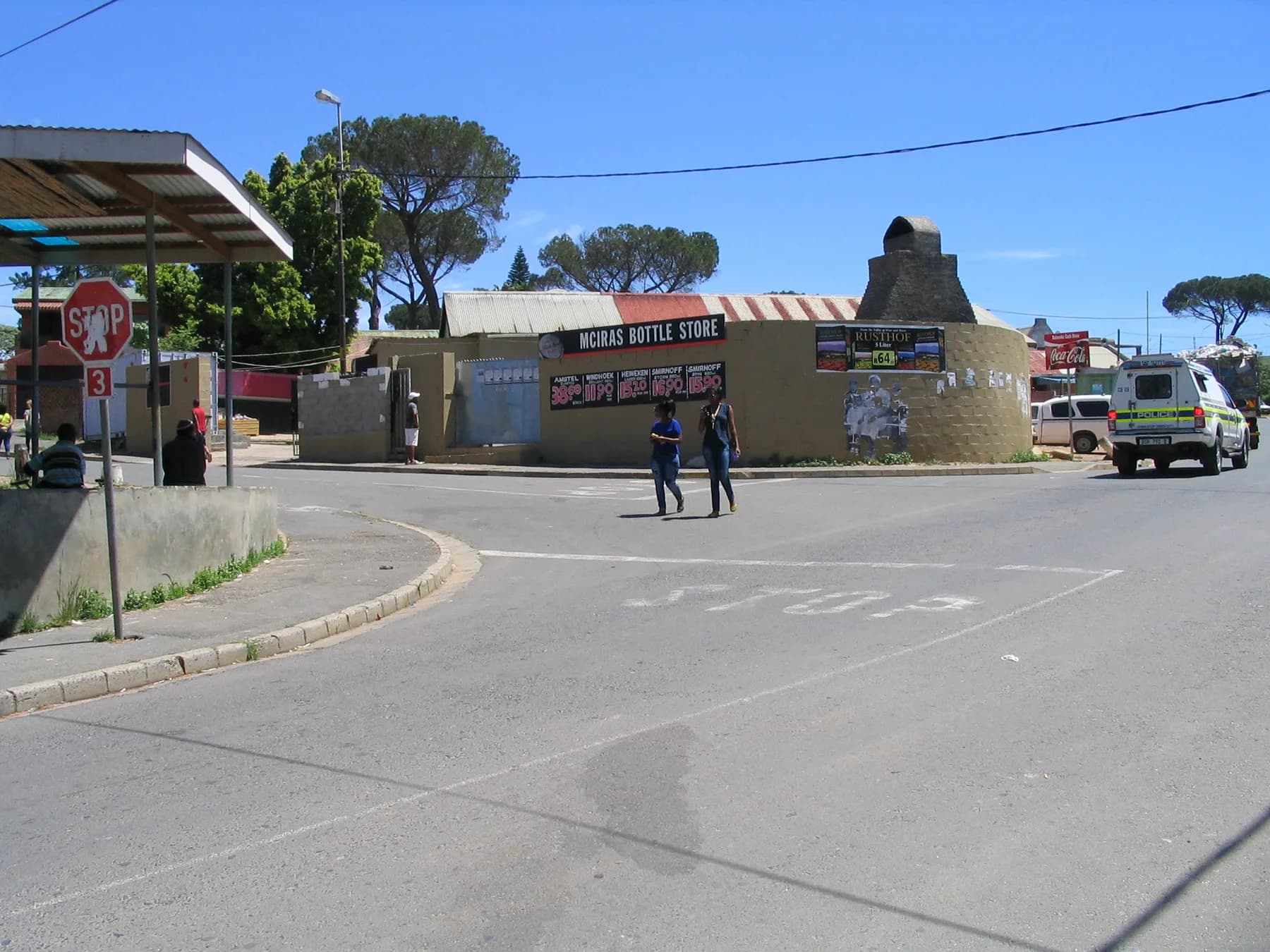 Two people crossing an intersection beside a corner bottle store