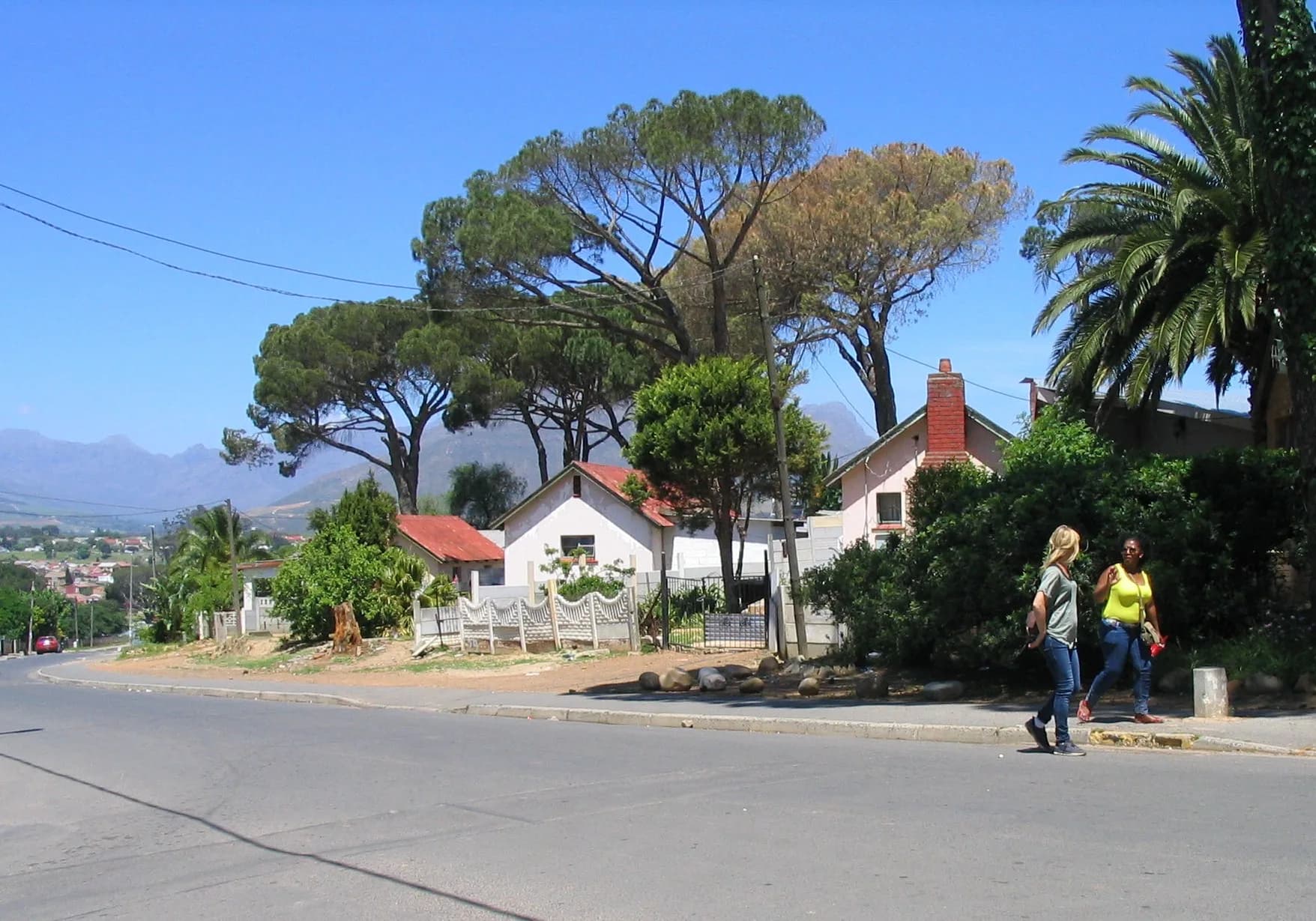 Two women walking together up a Kayamandi street in the sun