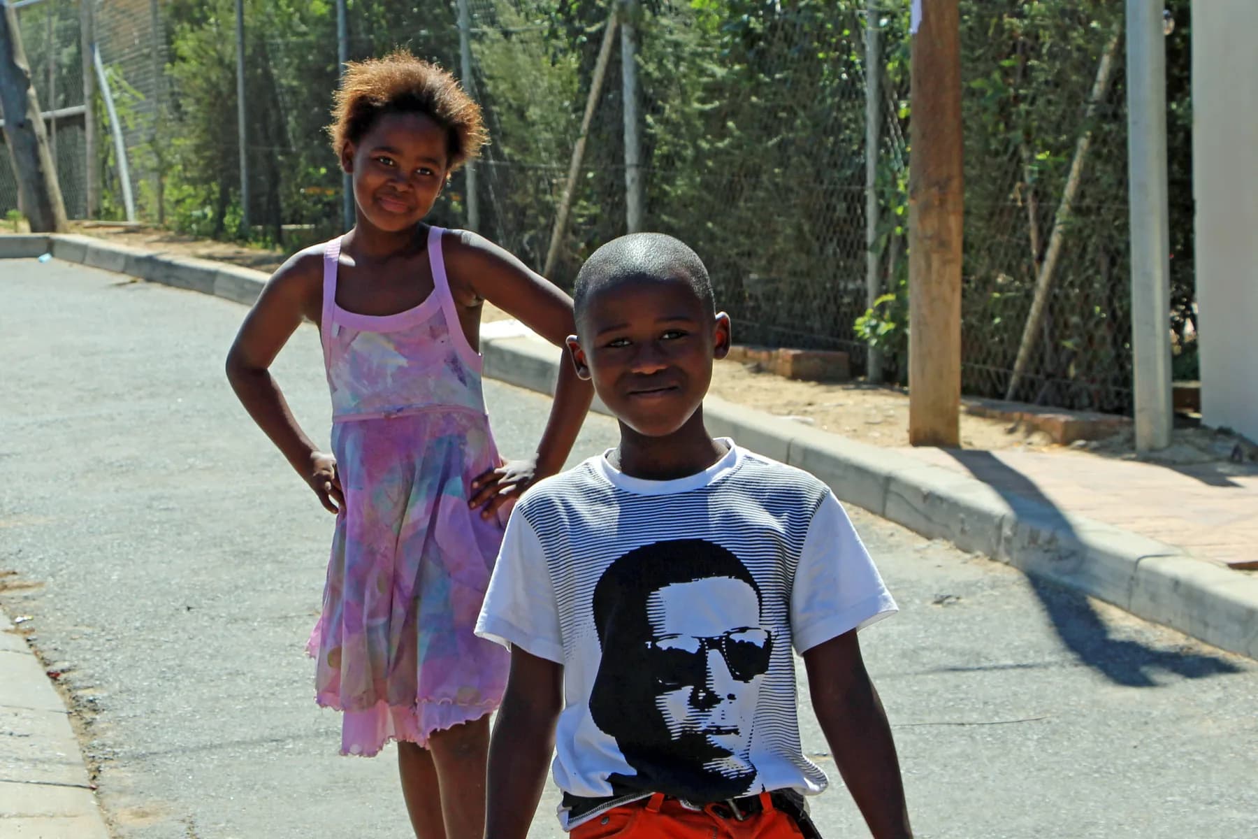 Two children standing together in the sun on a Kayamandi street