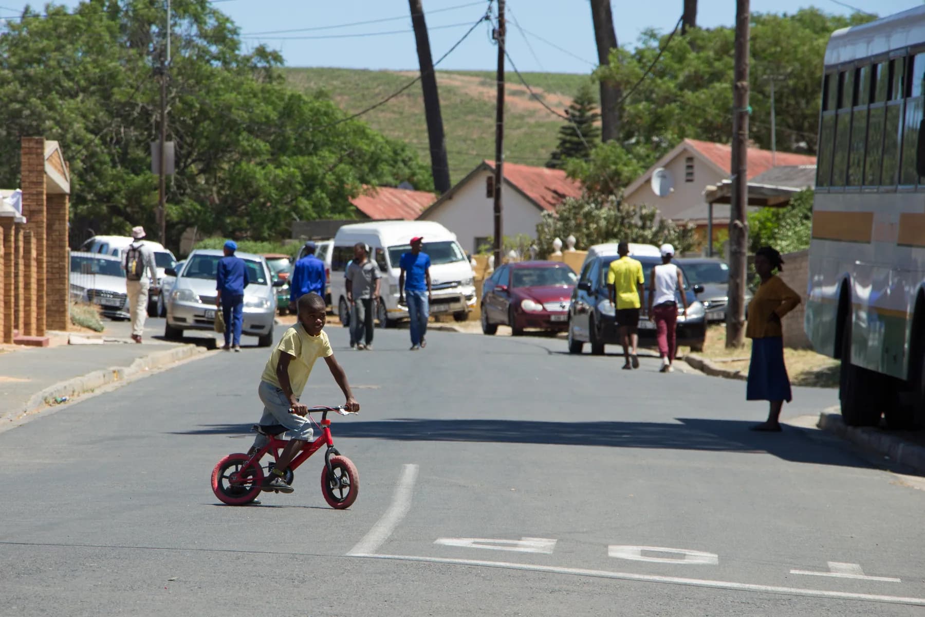 A small boy riding a red bicycle down the middle of the street