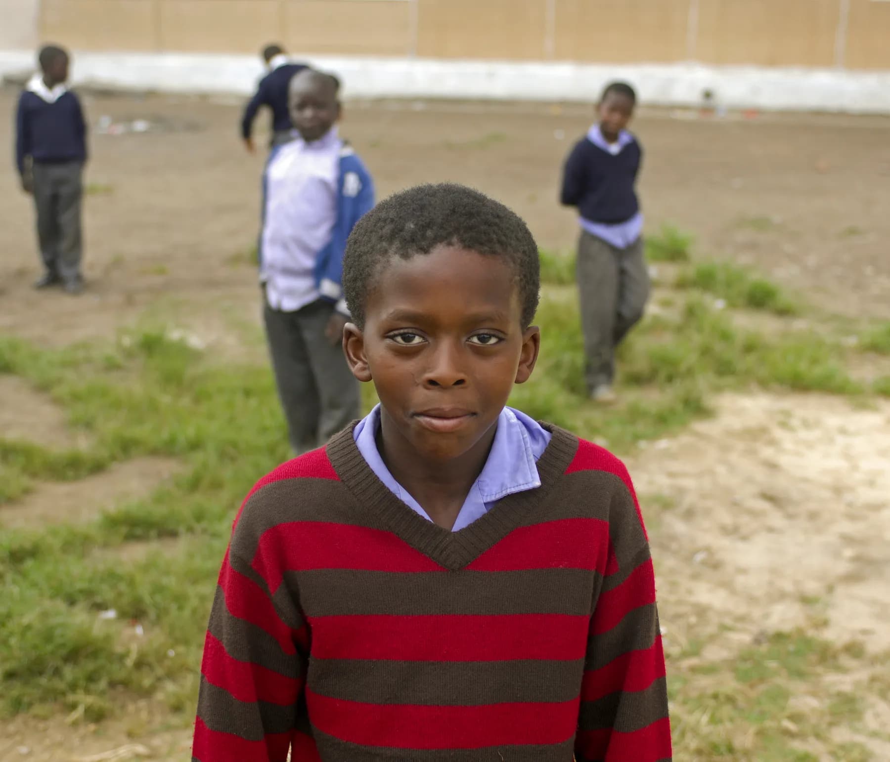 A boy in his school jersey looking straight at the camera, classmates on the ground behind him