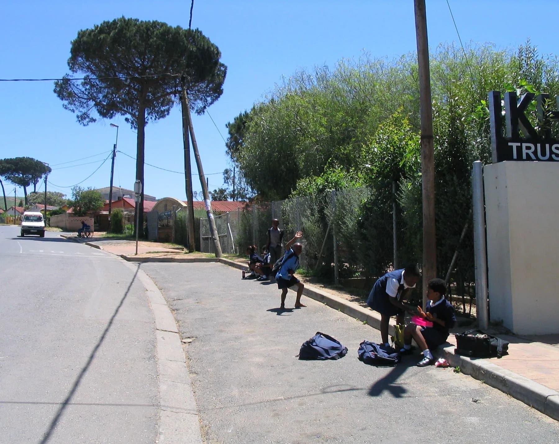 Schoolchildren sitting on the kerb with their bags beside them