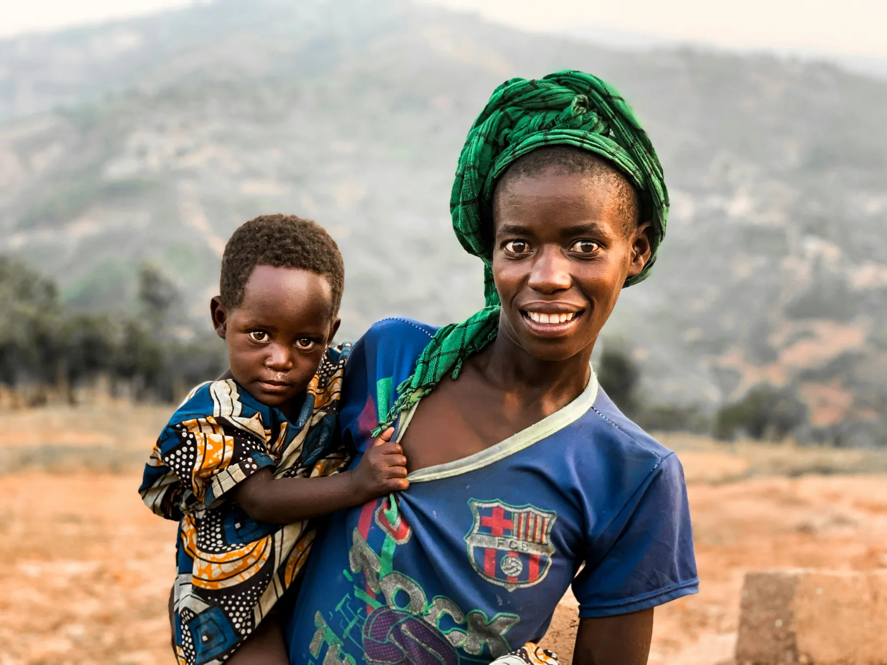 A woman carrying a small child on her hip, smiling at the camera