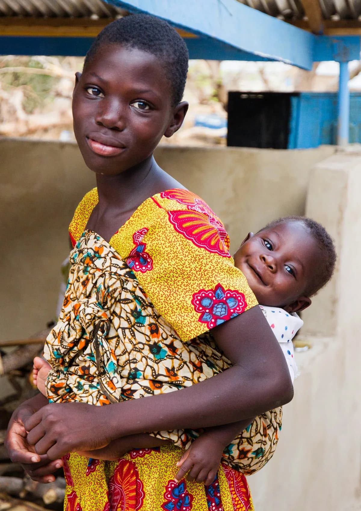 A girl carrying a baby on her back, both looking at the camera